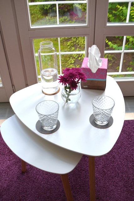 Zwei weiße Beistelltische mit Wasserkaraffe, Gläsern, Blumen und Taschentüchern vor einer Terrassentür